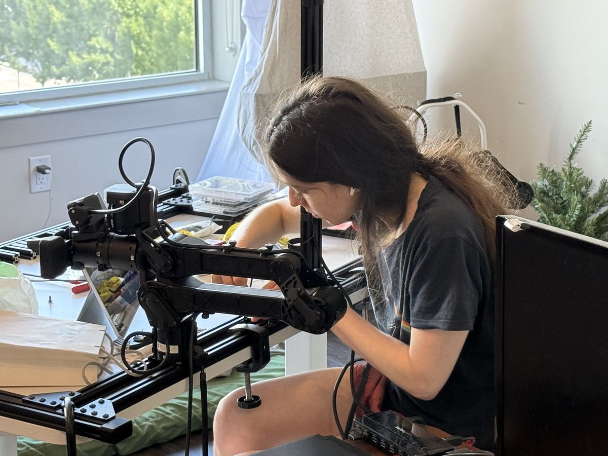 Katharine Henry adjusting the robot arm on its rig beside a sunny window.